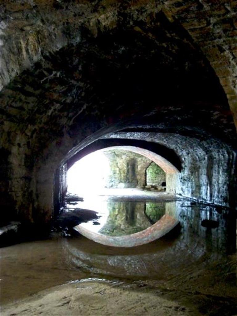 A stone tunnel in Frome, with still water reflecting the arched opening onto daylight.